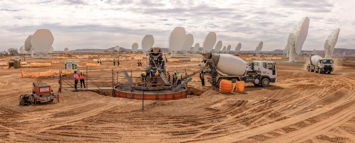 Panoramic view of satellite dish construction site with equipment and workers in desert landscape.