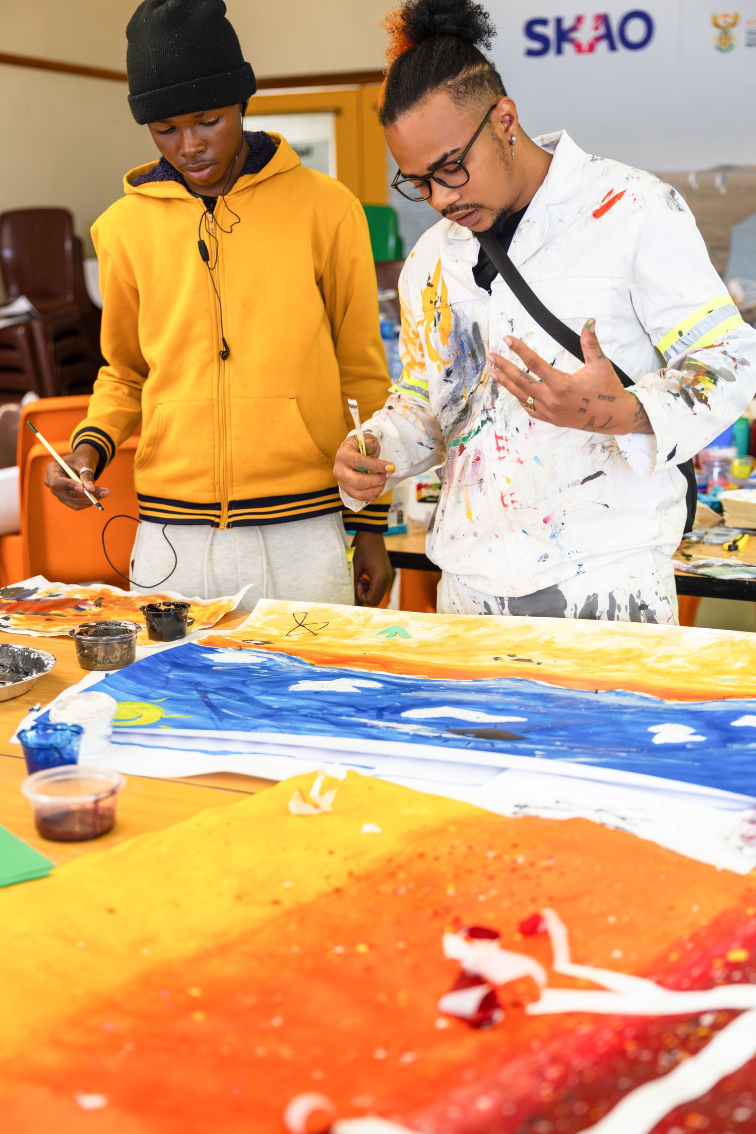 Artists working on a vibrant painting with blue and orange colors in a studio setting.