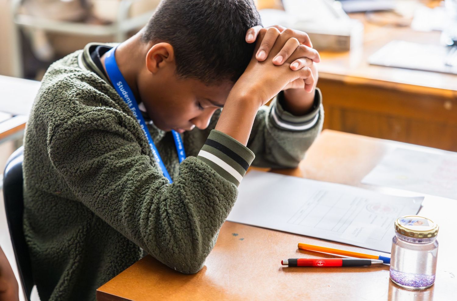 Students concentrating on their work at wooden desks in a classroom environment.