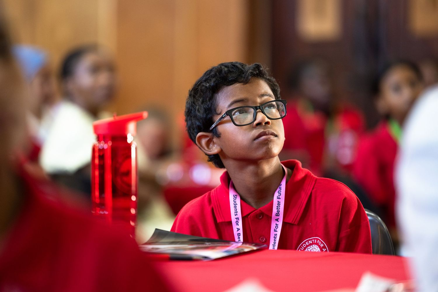 Student in red attire listens attentively during an educational session.