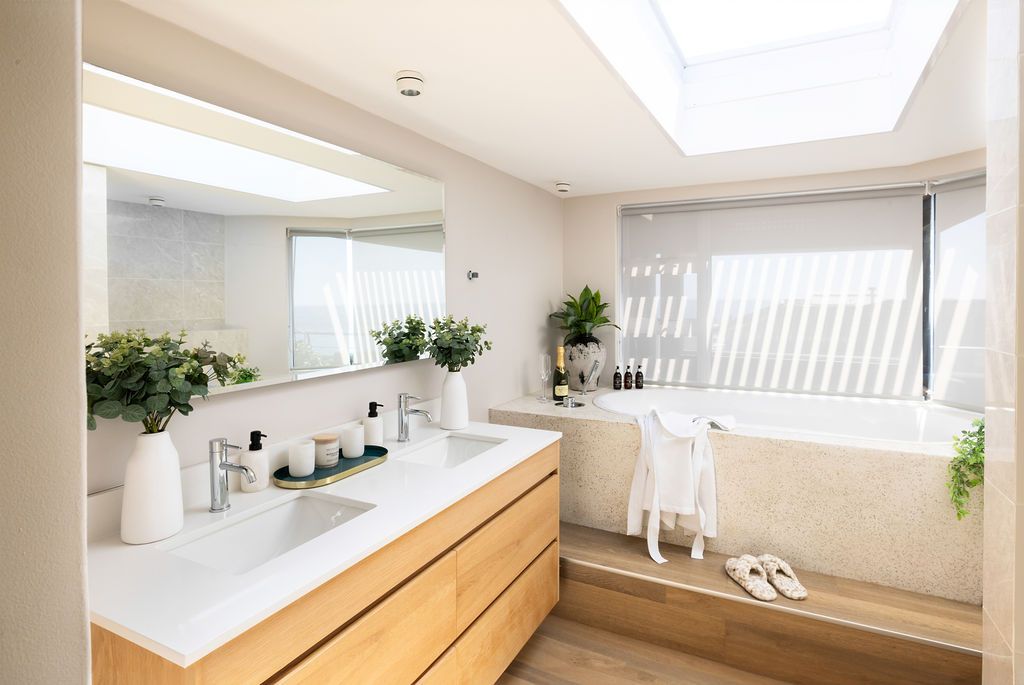 Modern bright bathroom interior with wooden vanity, white countertop, large mirror and natural light from skylight.