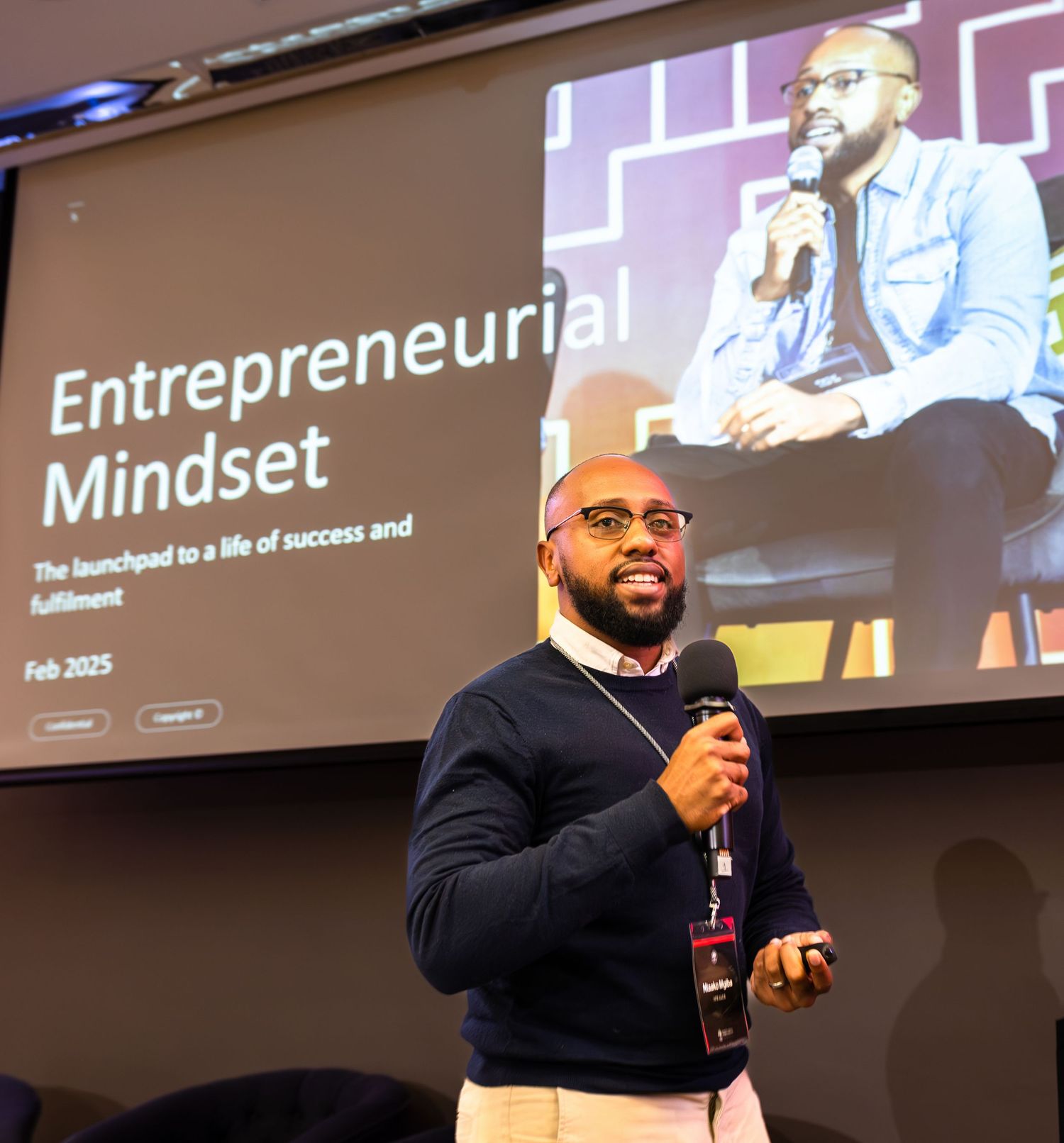 A presenter speaks passionately on stage during an entrepreneurship conference.