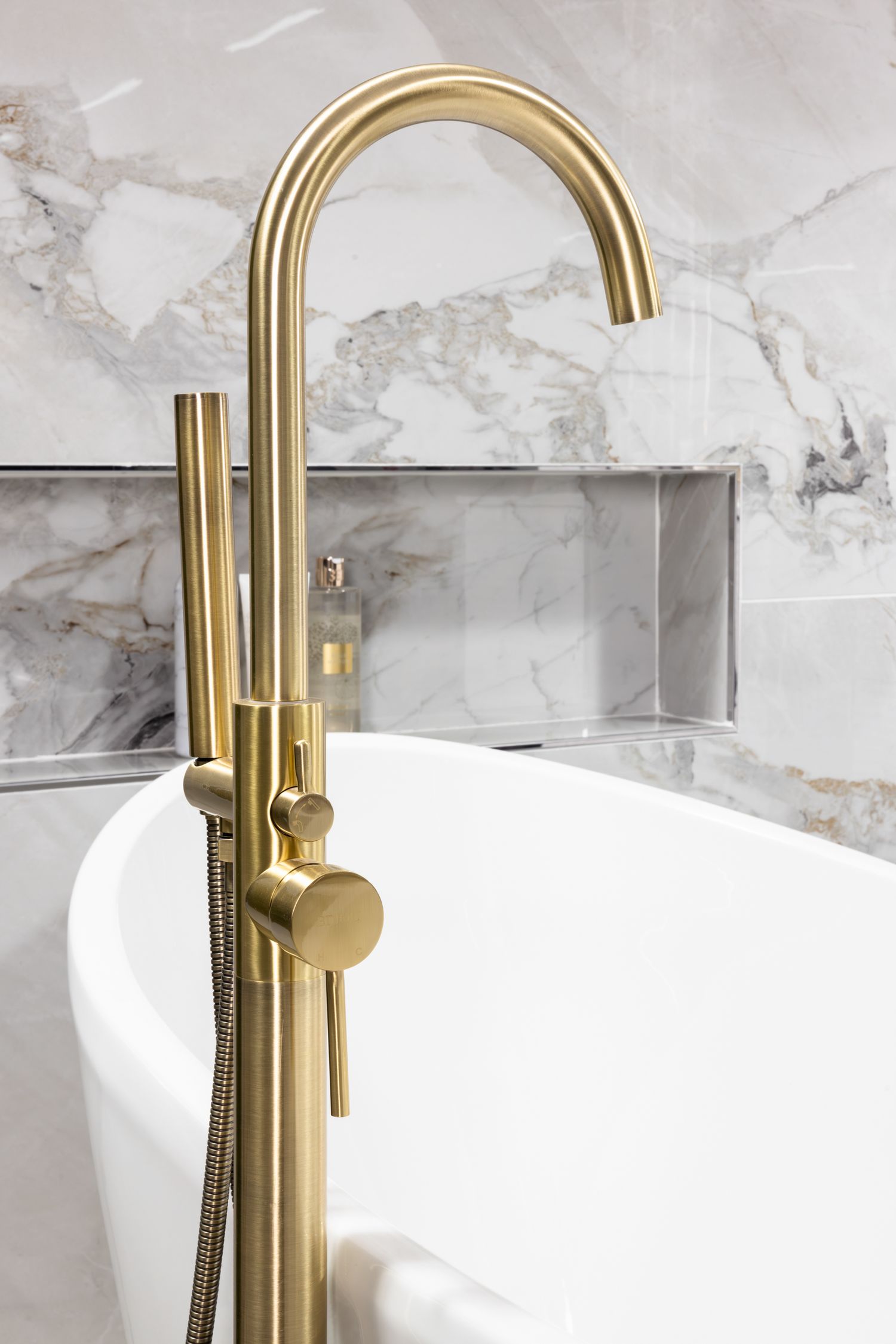 Close-up of luxury gold freestanding bathtub faucet against marble wall background.