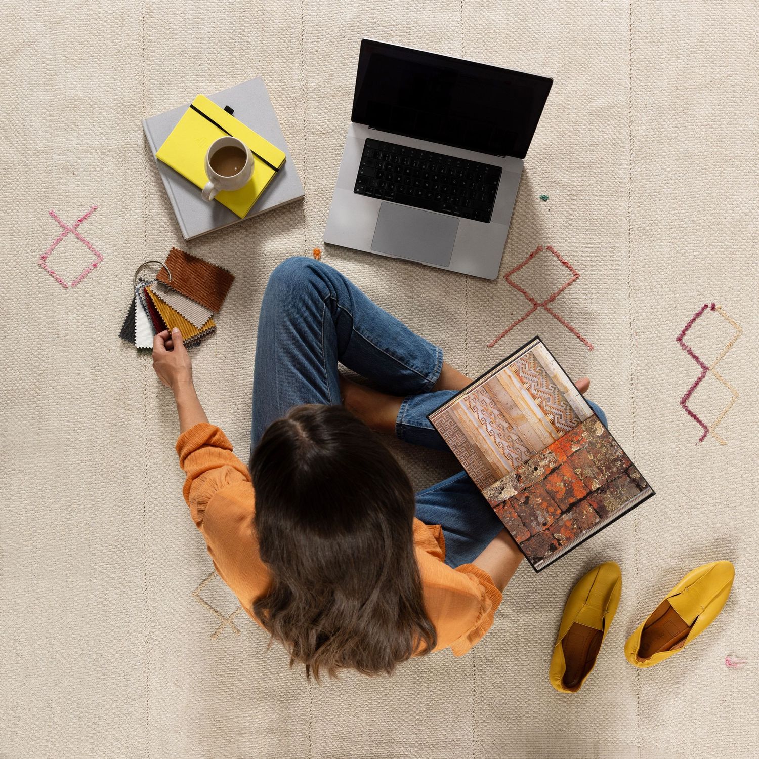 Overhead view of someone working on laptop with coffee and yellow shoes on carpet with geometric pattern design.