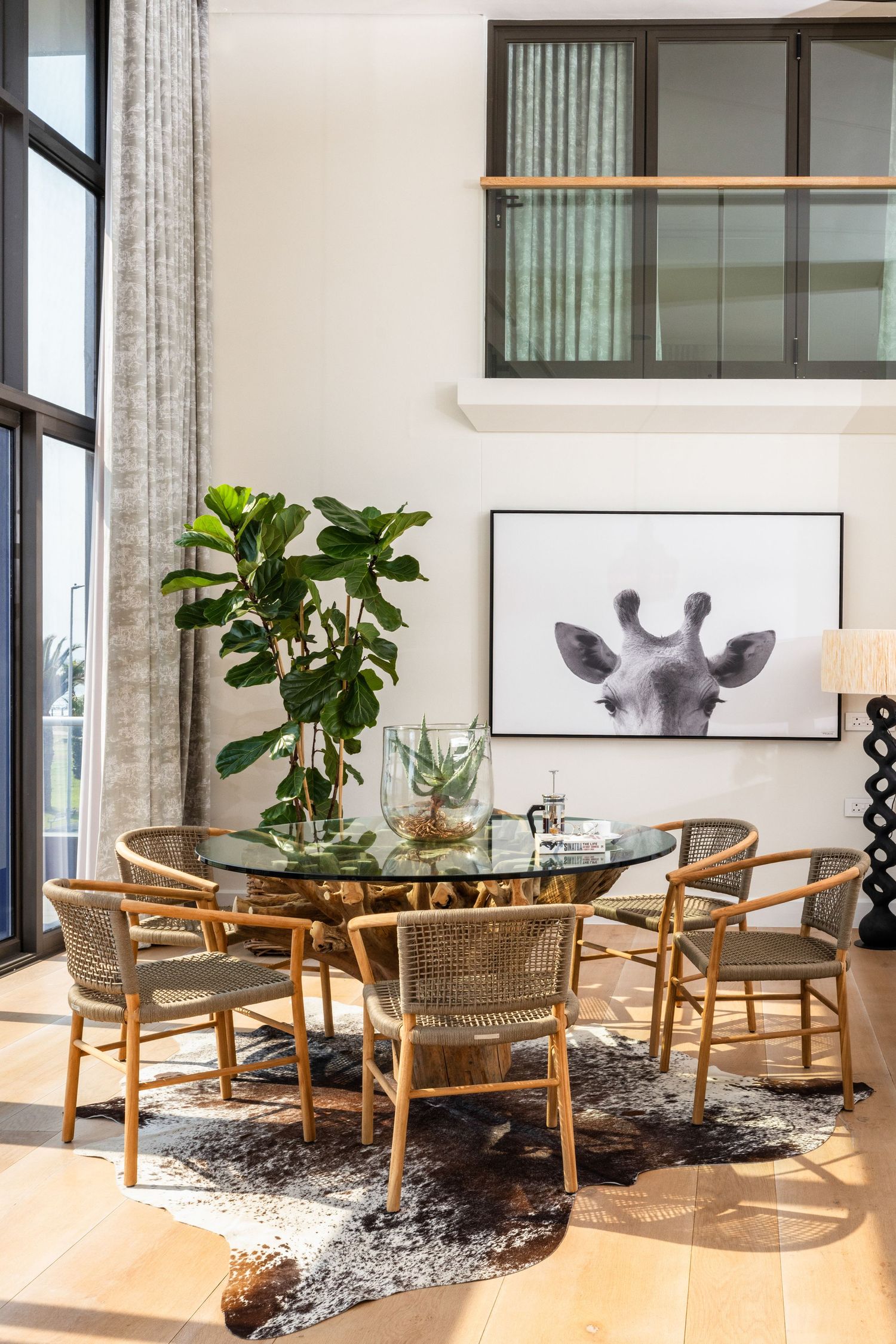 Modern living room features rattan chairs, indoor plants, and black and white animal artwork in a bright, airy space.