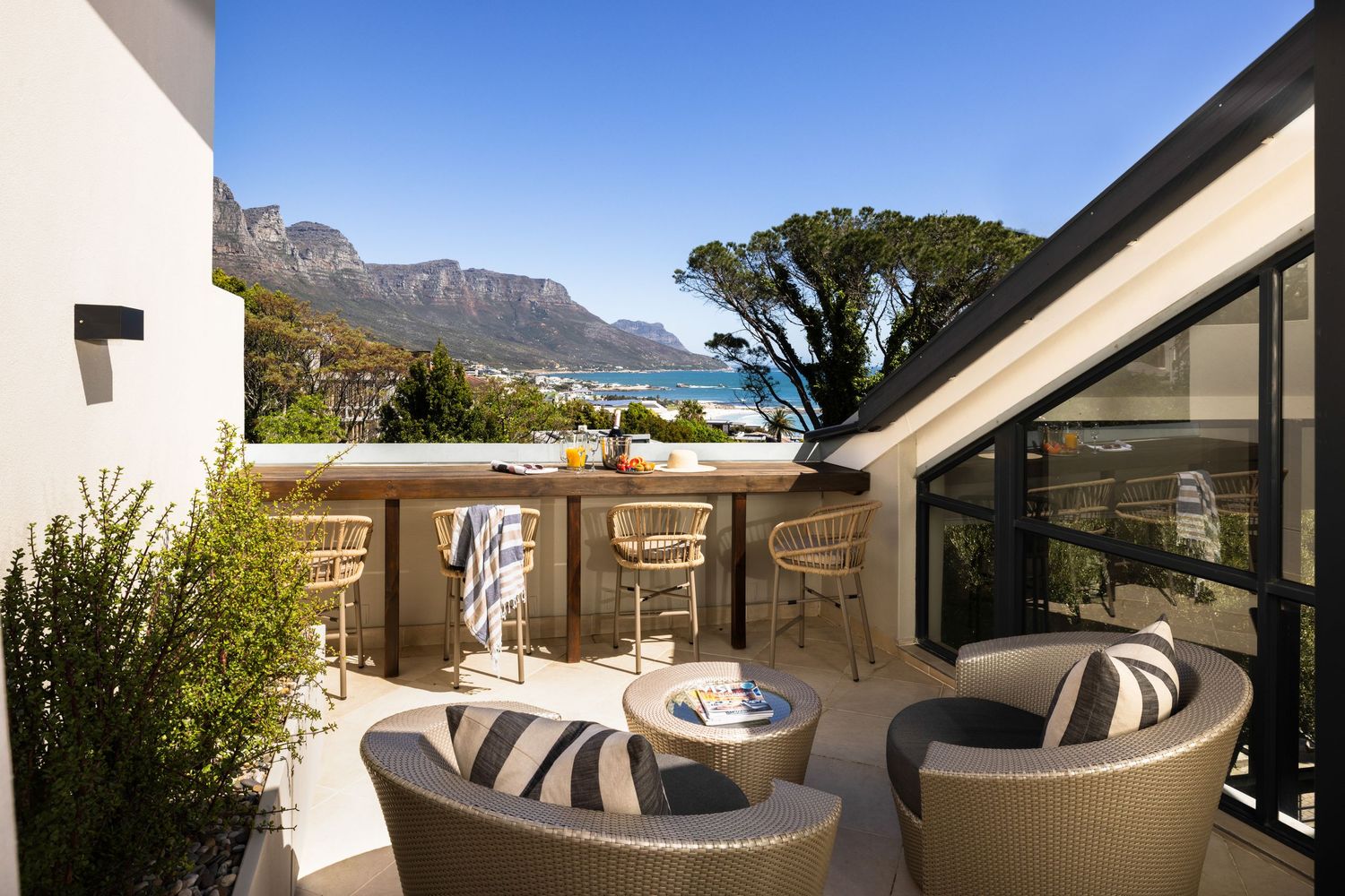 Luxurious outdoor terrace with modern furniture overlooking Cape Town's mountains and coastline on a sunny day.