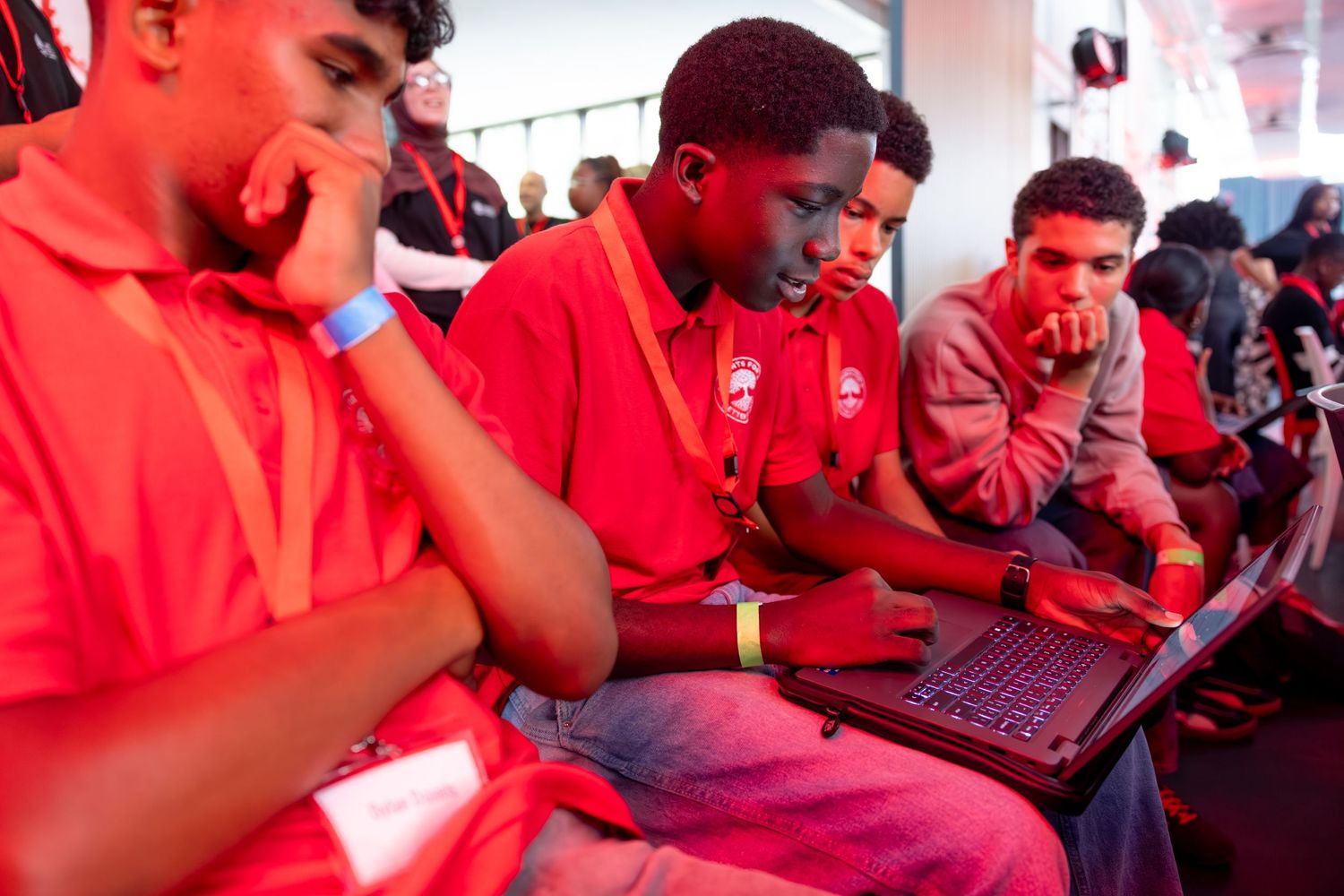 Students in red uniforms work on laptops during an educational event.