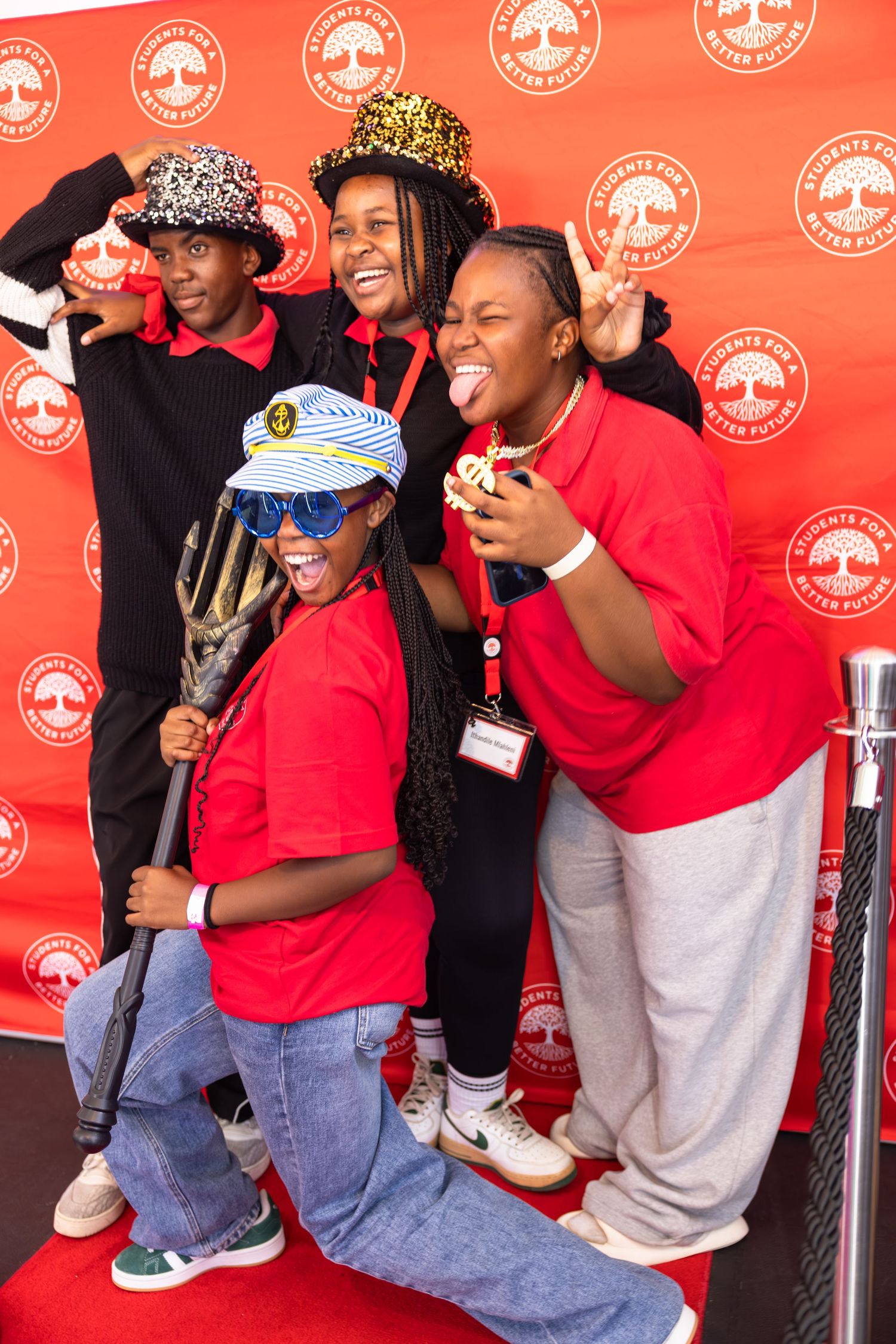 A group wearing red shirts smiles and laughs together against a backdrop with repeating logo patterns.