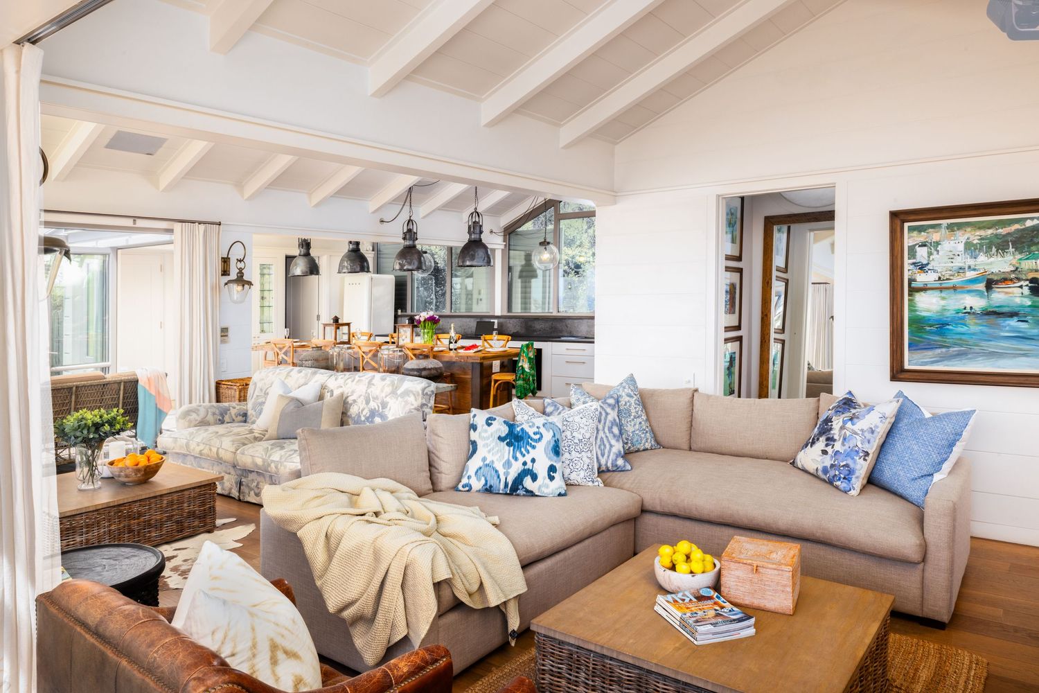 Modern coastal living room with white beamed ceiling, plush seating, and ocean views through large windows.