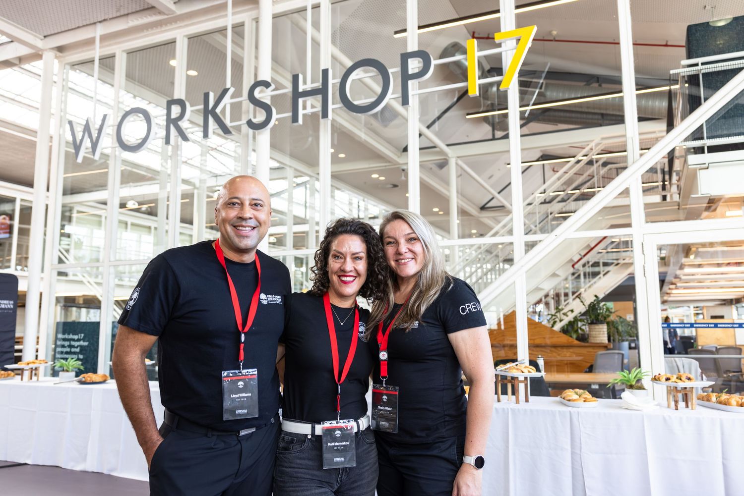 Workshop participants in dark attire gather and smile together in a bright indoor space.