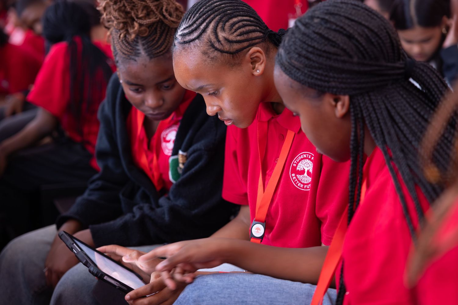 Students wearing red shirts focus on their devices during a group learning session.