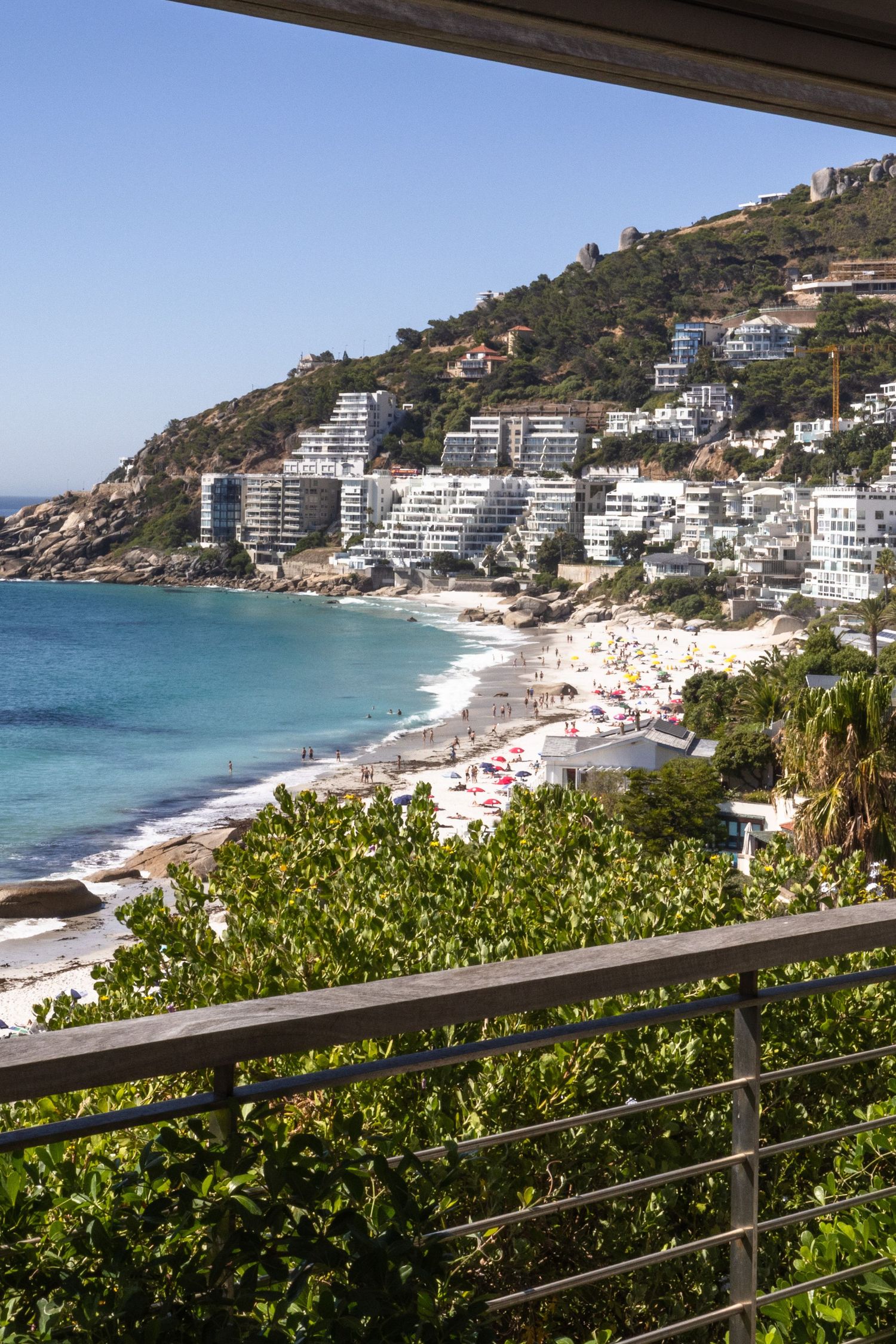Luxurious beachfront apartments nestled on a hillside overlooking turquoise waters and a sandy beach in Cape Town.