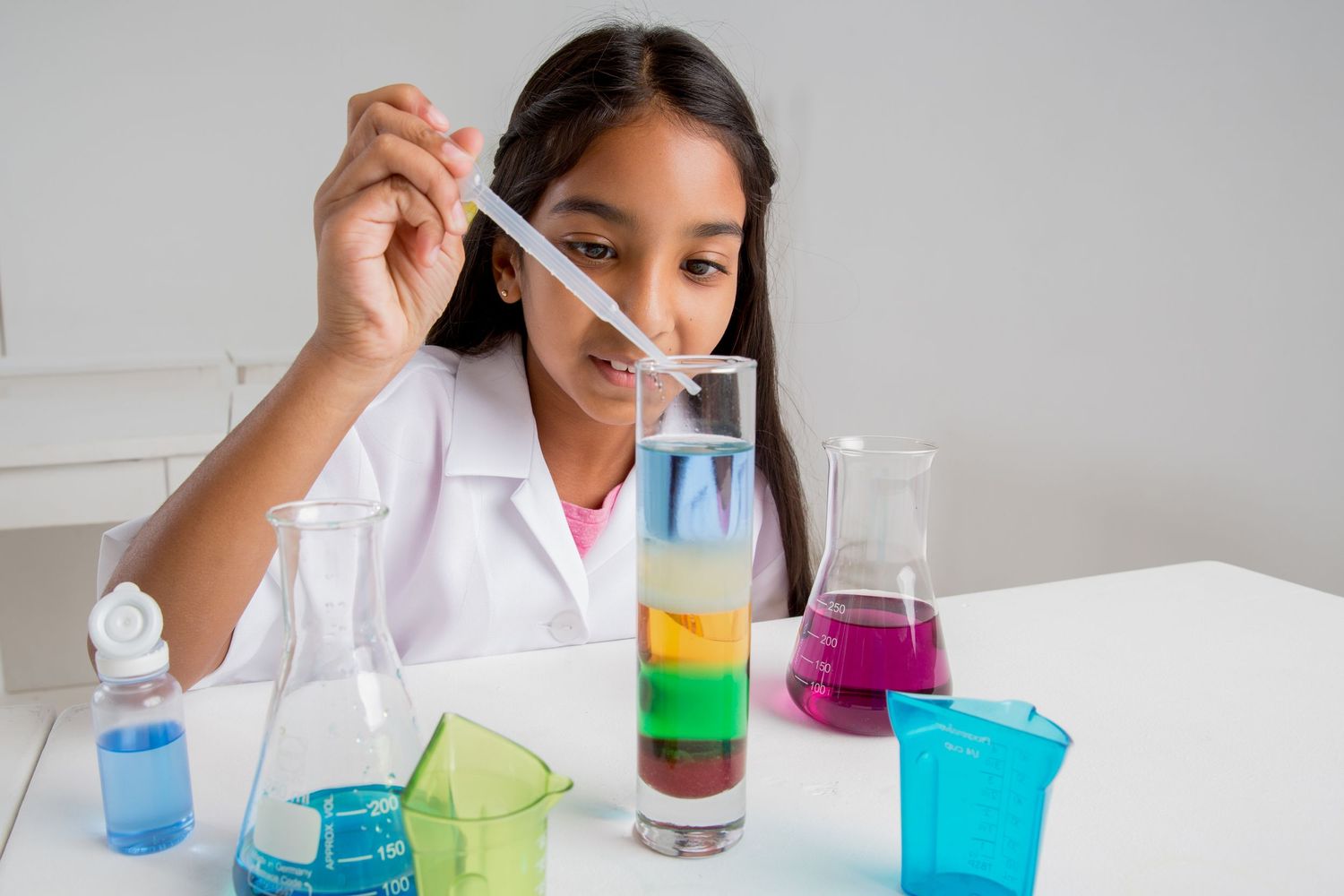 Student conducts density experiment with layered colorful liquids in clear glass tube.
