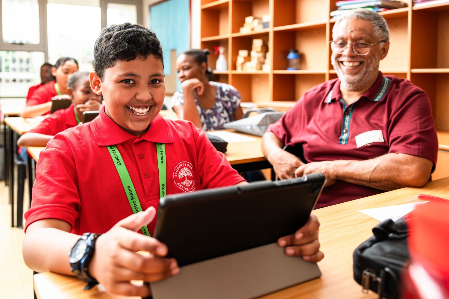 Two students collaborate while using digital tablet in classroom setting.