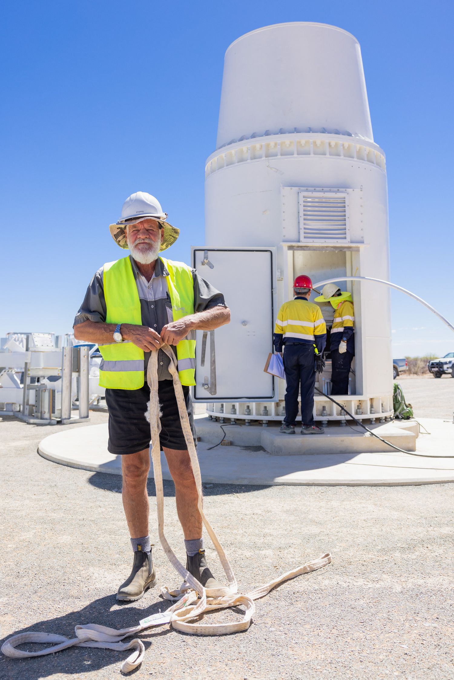 Field technicians performing maintenance checks around white dome structures in a desert setting.