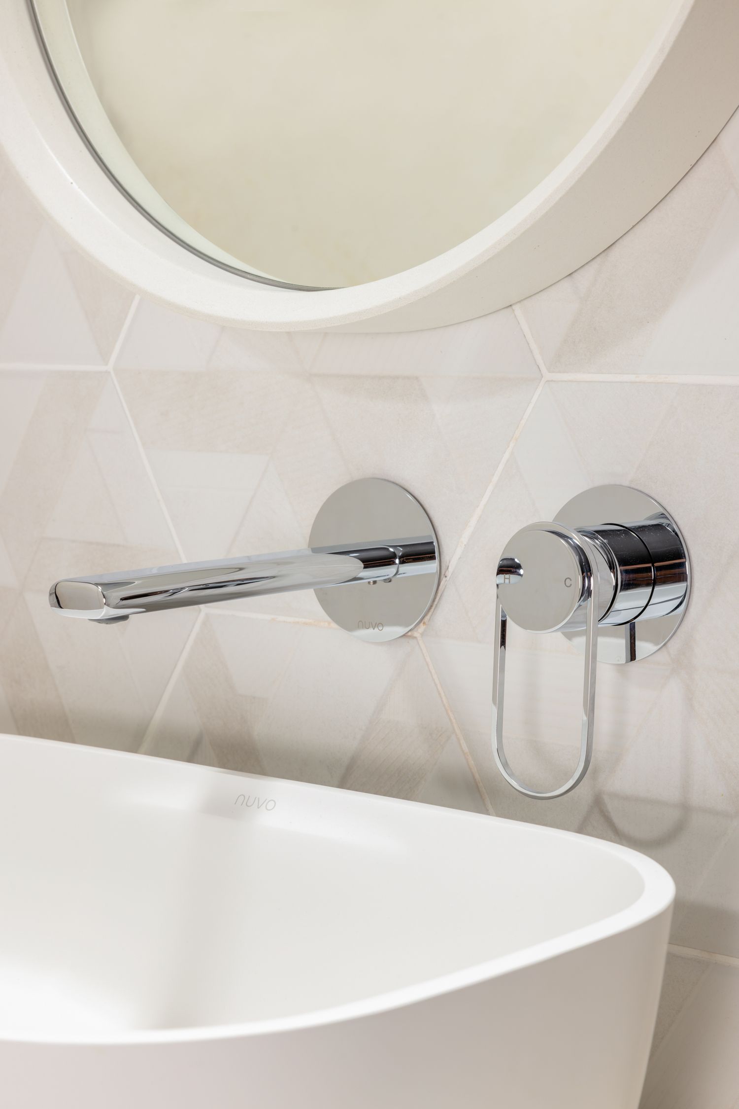 Minimalist wall-mounted chrome faucet and white vessel sink below round mirror.