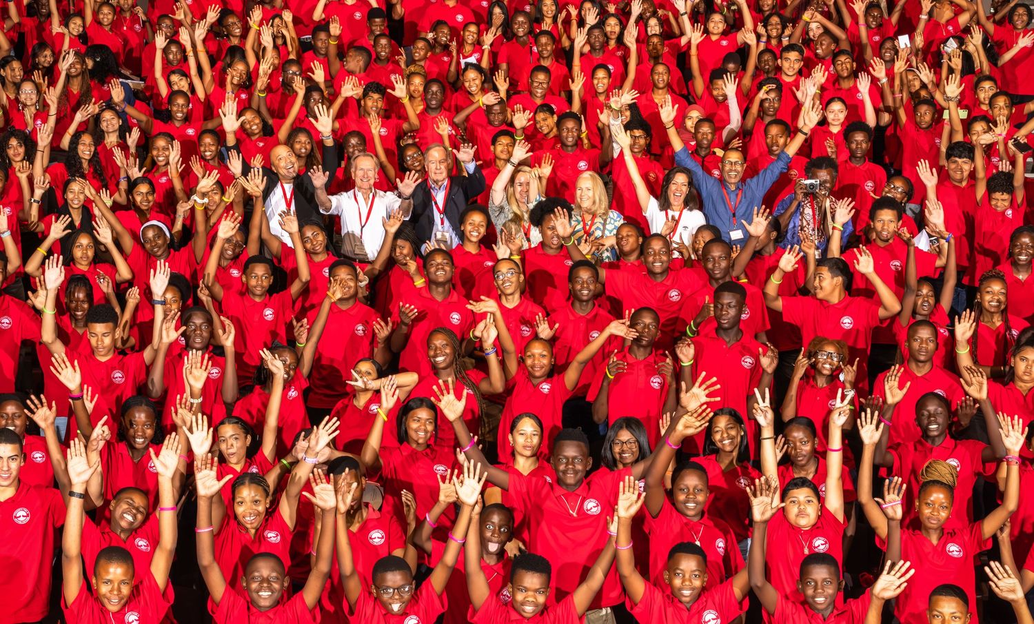 Enthusiastic crowd in red shirts with raised arms celebrating during an event.