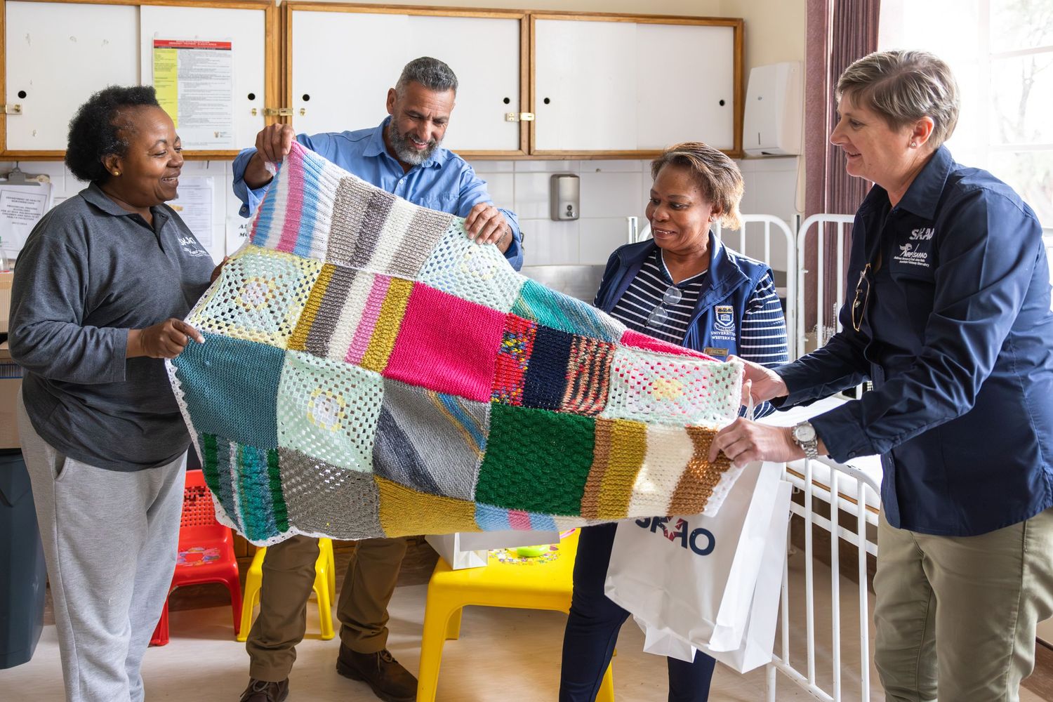 A group displaying a colorful patchwork quilt in an office setting.