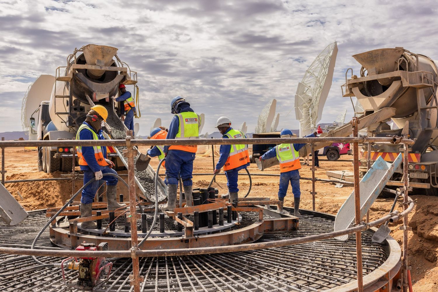 Workers in safety gear pouring concrete at satellite dish construction site.