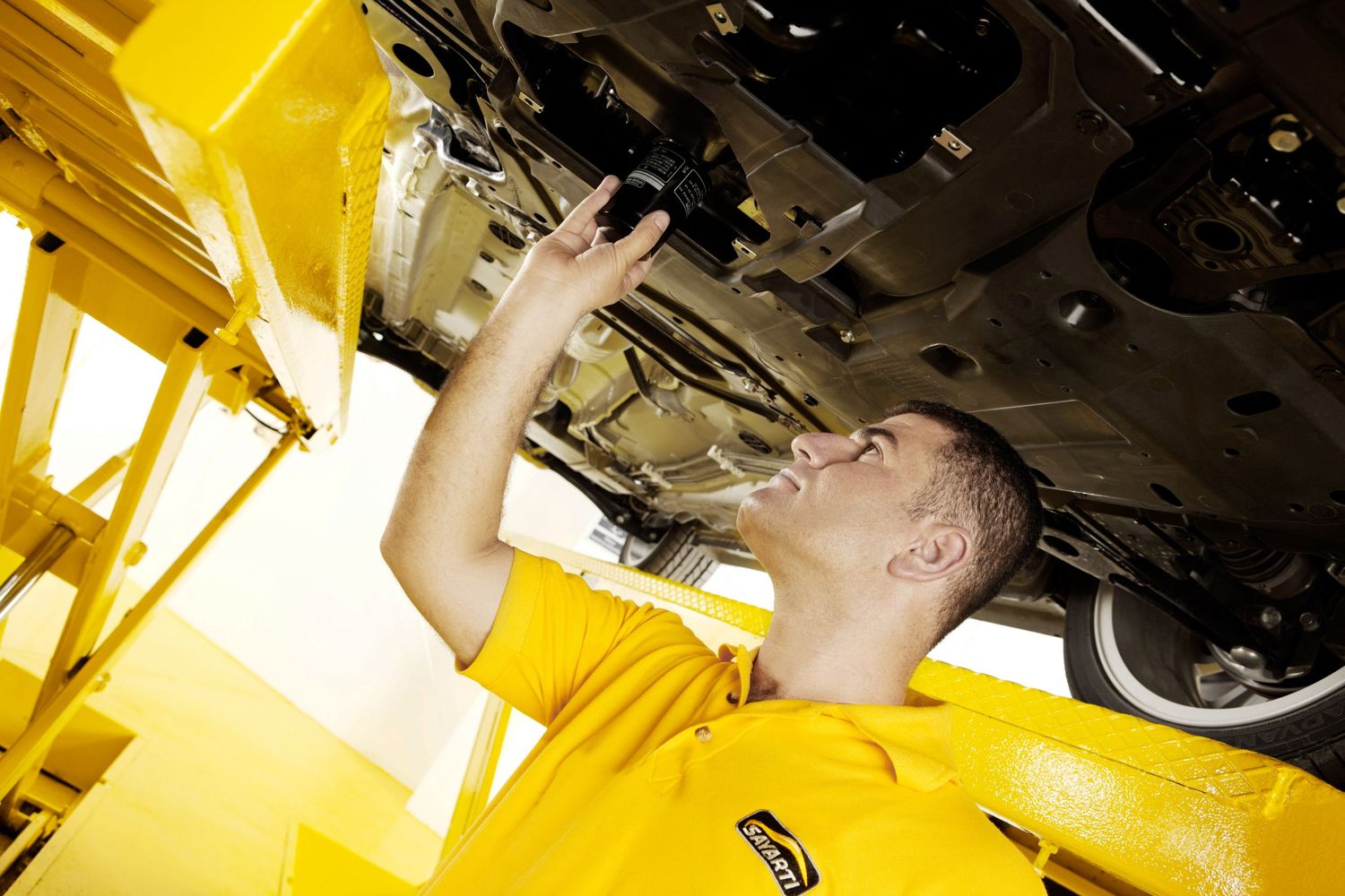 Auto technician in yellow uniform performing maintenance check under vehicle.