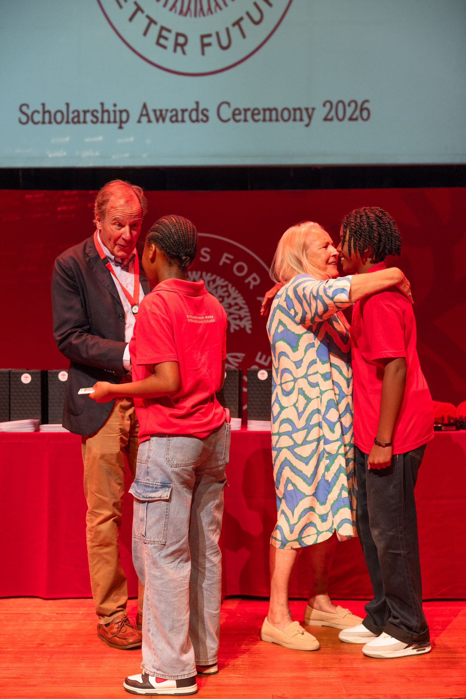 Scholarship awards ceremony showing students receiving recognition on a red-lit stage.