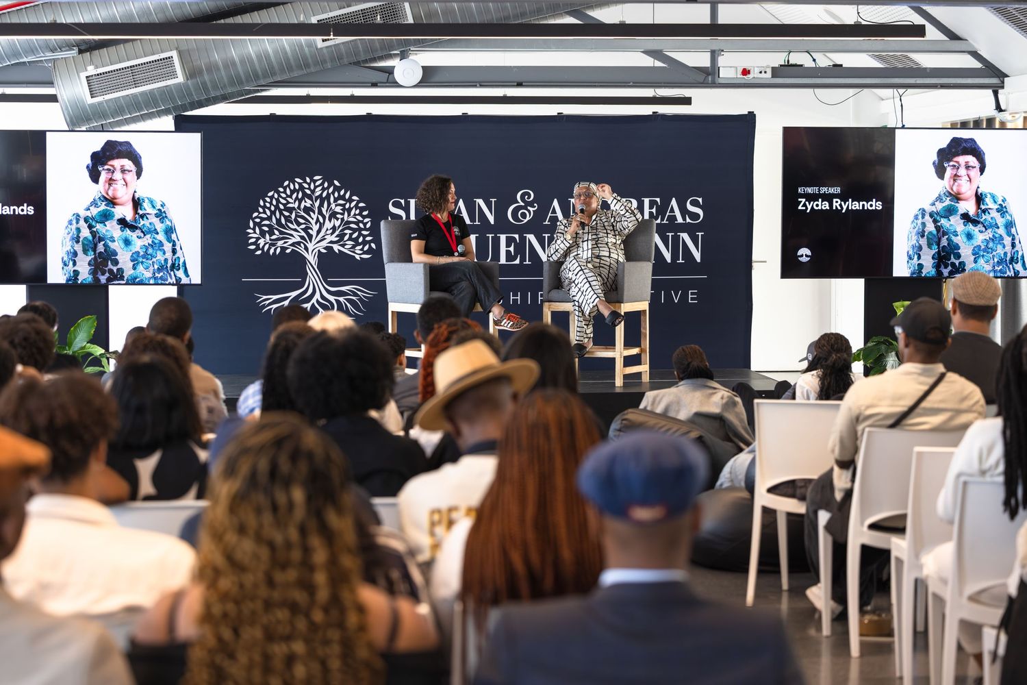 Wide shot of conference room setup with audience facing panel discussion stage and branded backdrop.