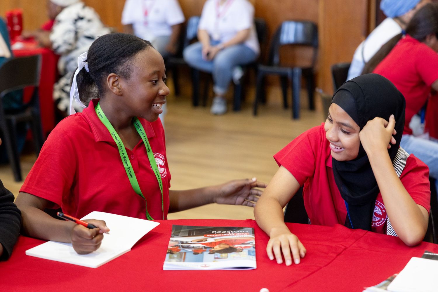 Students working together at tables with red tablecloths during a learning session.