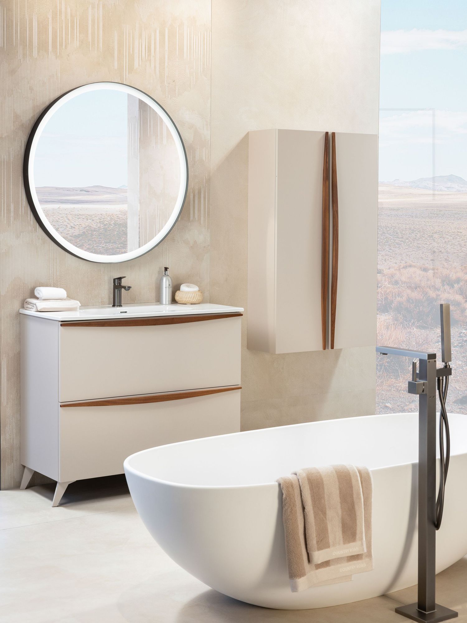 Modern luxury bathroom with freestanding white tub, floating vanity, and circular mirror overlooking desert landscape.