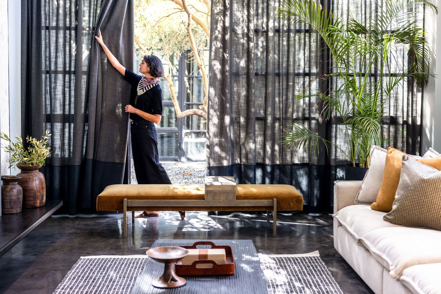 Stylish modern living room interior with black curtains, bench seating, and decorative pillows in natural lighting.