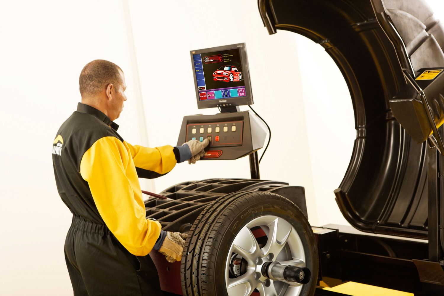 Technician operating tire balancing machine with digital display at auto service center.