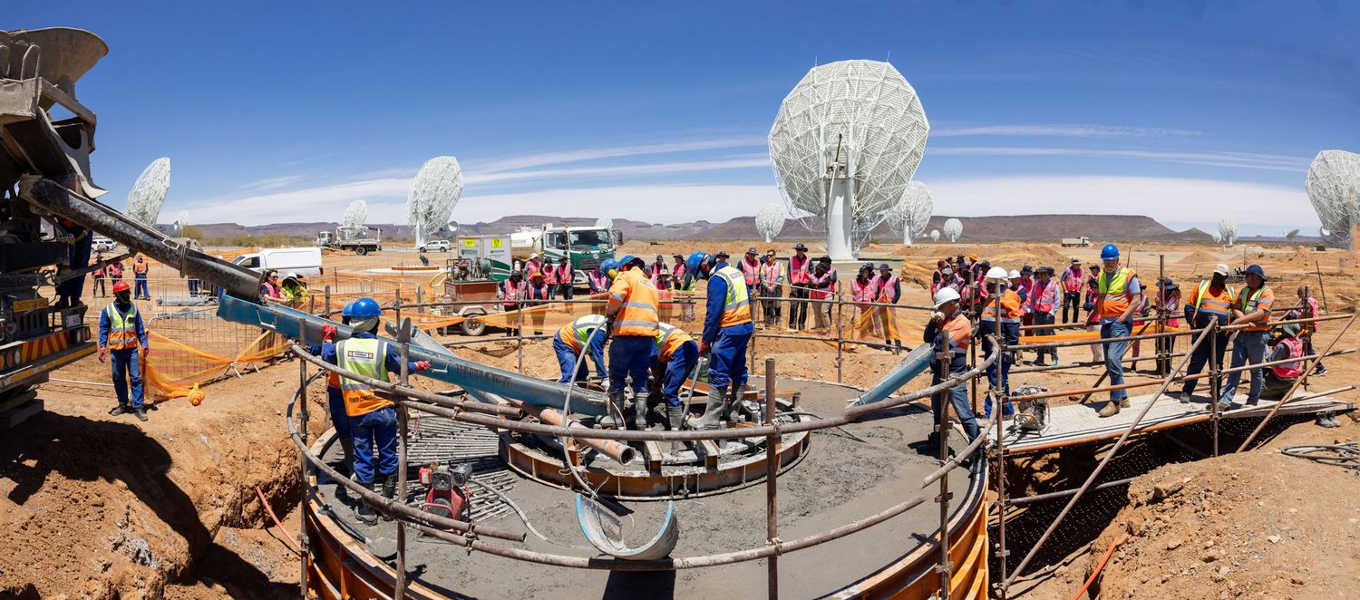 Large white satellite dishes stand against a desert landscape with crowds of visitors touring the facility.