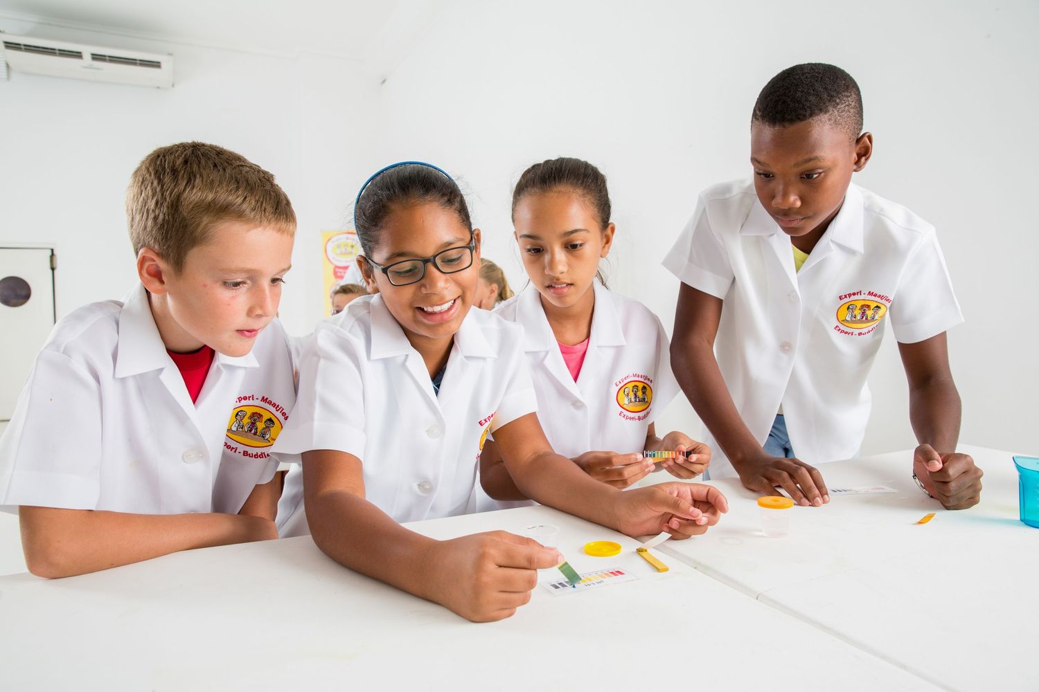 Students collaborate on a science experiment while wearing white lab coats and safety gear.