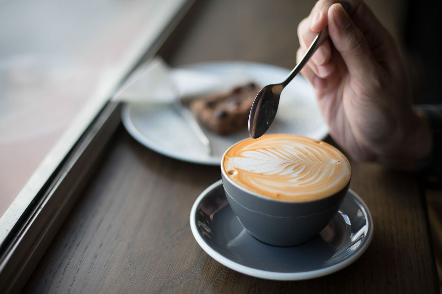Series of detailed latte art being poured into dark ceramic cups.