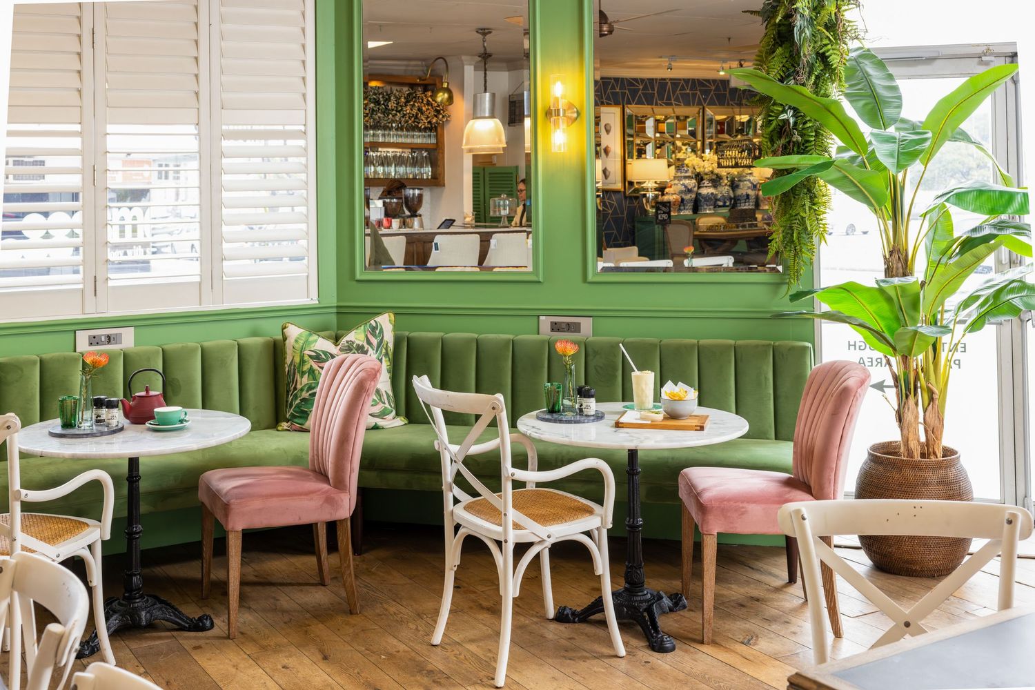 Modern cafe interior with green wainscoting, pink chairs, and tropical plants creating a cozy dining atmosphere.