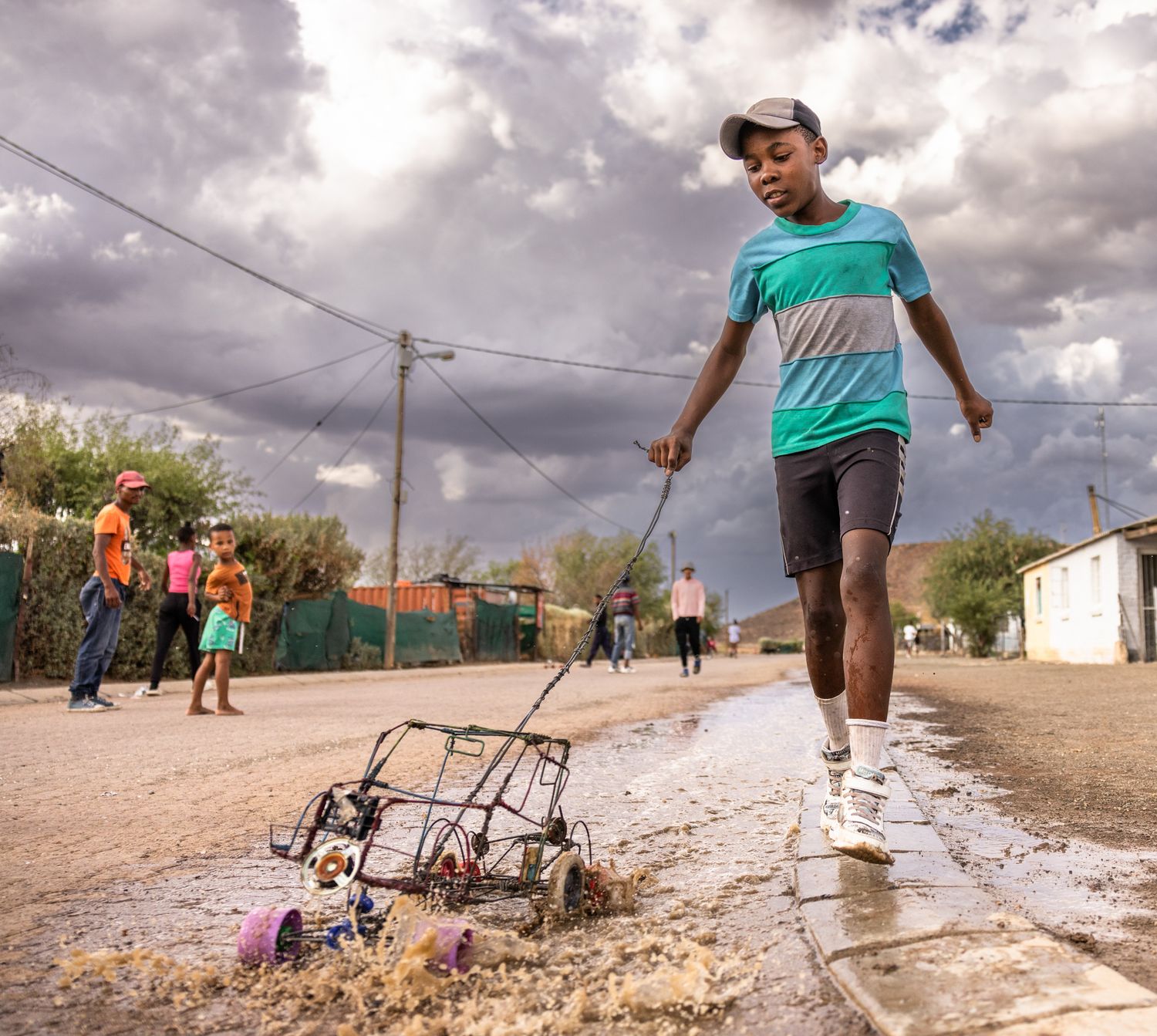 People navigating flooded streets and muddy terrain in front of basic residential buildings.