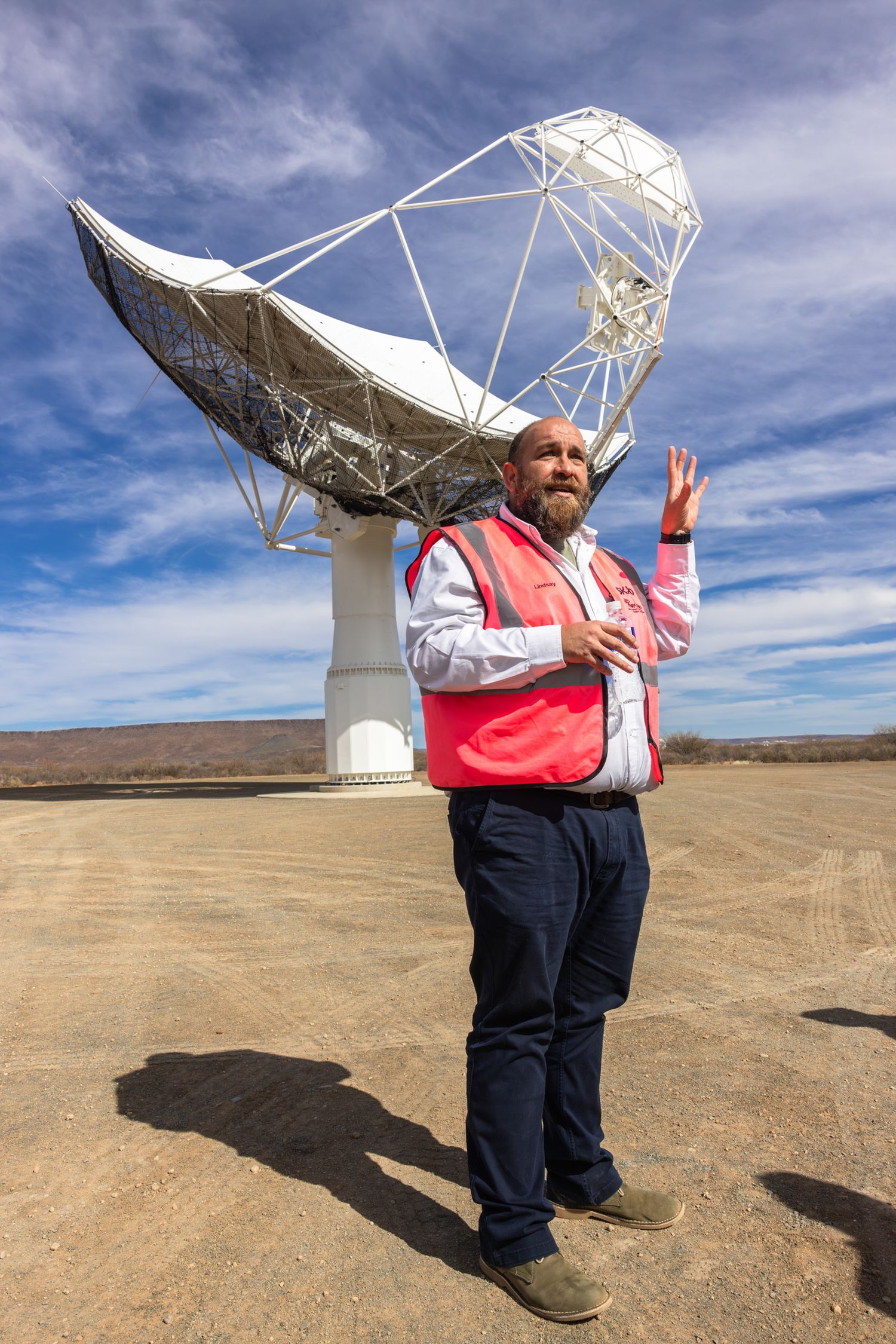 Large white radio telescope dish installation in desert setting with blue sky background.