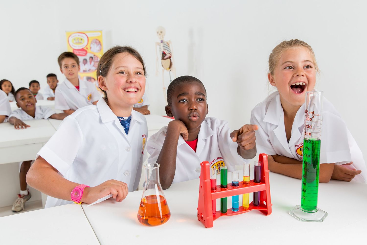 Students in white lab coats show excitement while conducting colorful chemistry experiments with test tubes in classroom.
