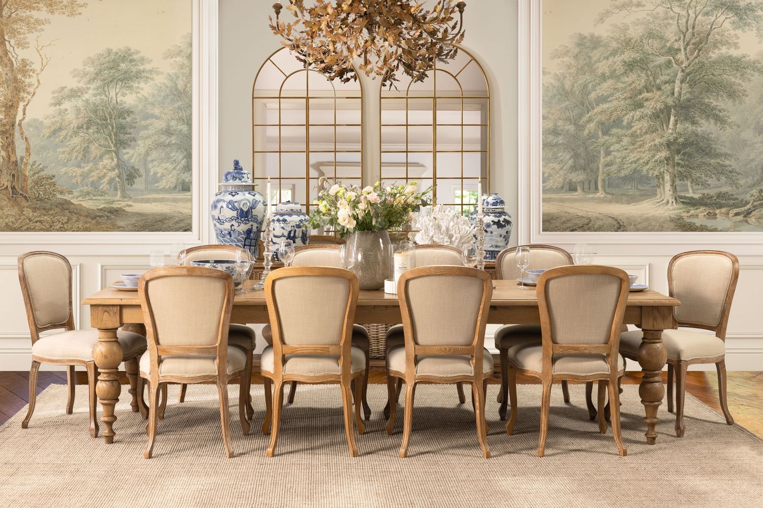 Elegant formal dining room with cream upholstered chairs, farmhouse table, crystal chandelier and pastoral wall murals.