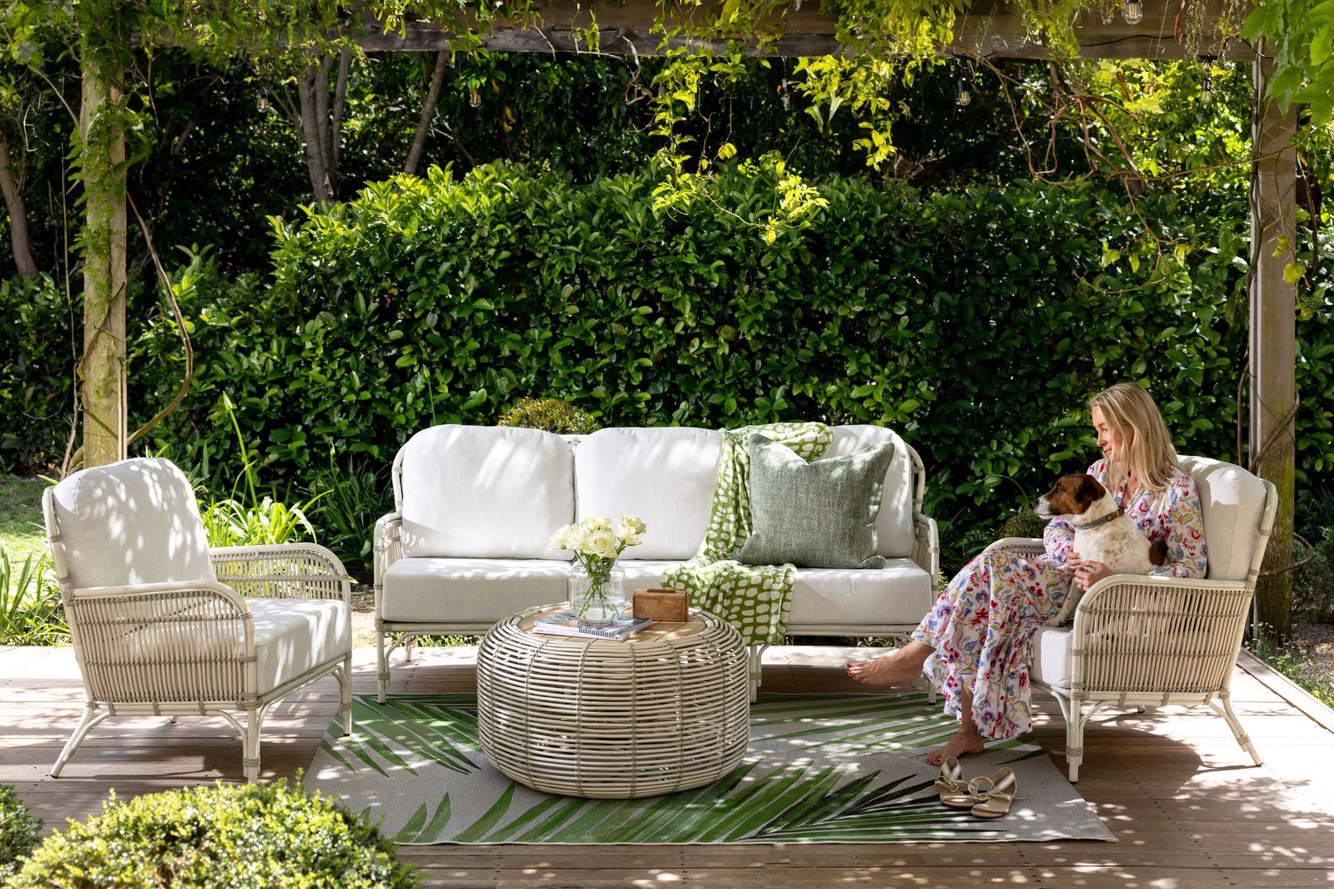 A serene outdoor garden patio with white cushioned furniture and lush greenery creating a tranquil atmosphere.