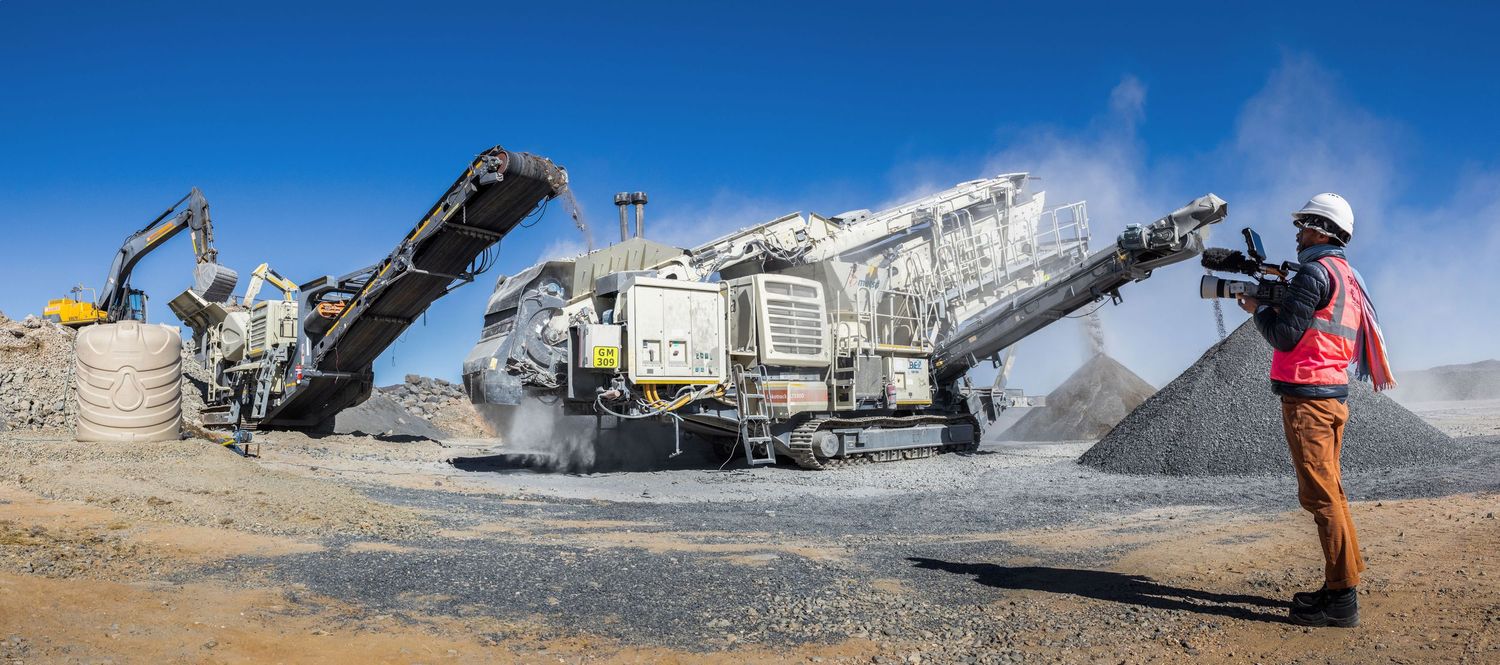 Industrial rock crusher and conveyor belt operating at a quarry site.