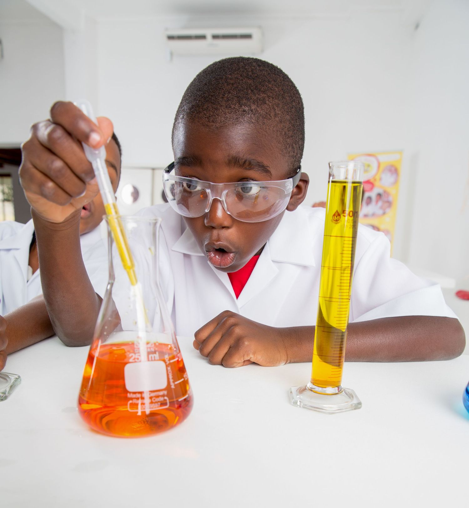 Student in safety glasses observes orange liquid in laboratory flask during science experiment.