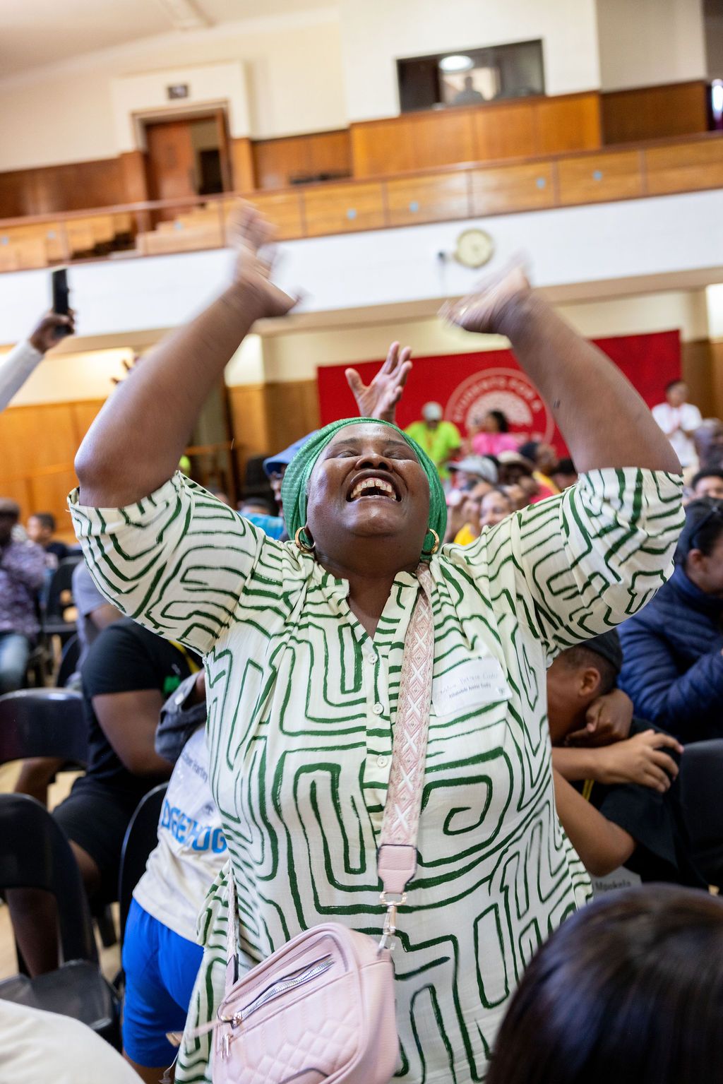 People in green patterned clothing laugh and gesture expressively during an indoor gathering.