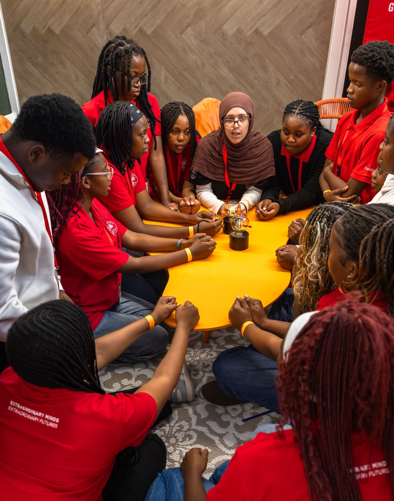 Students in red shirts gather around yellow tables for an engaging group activity session.