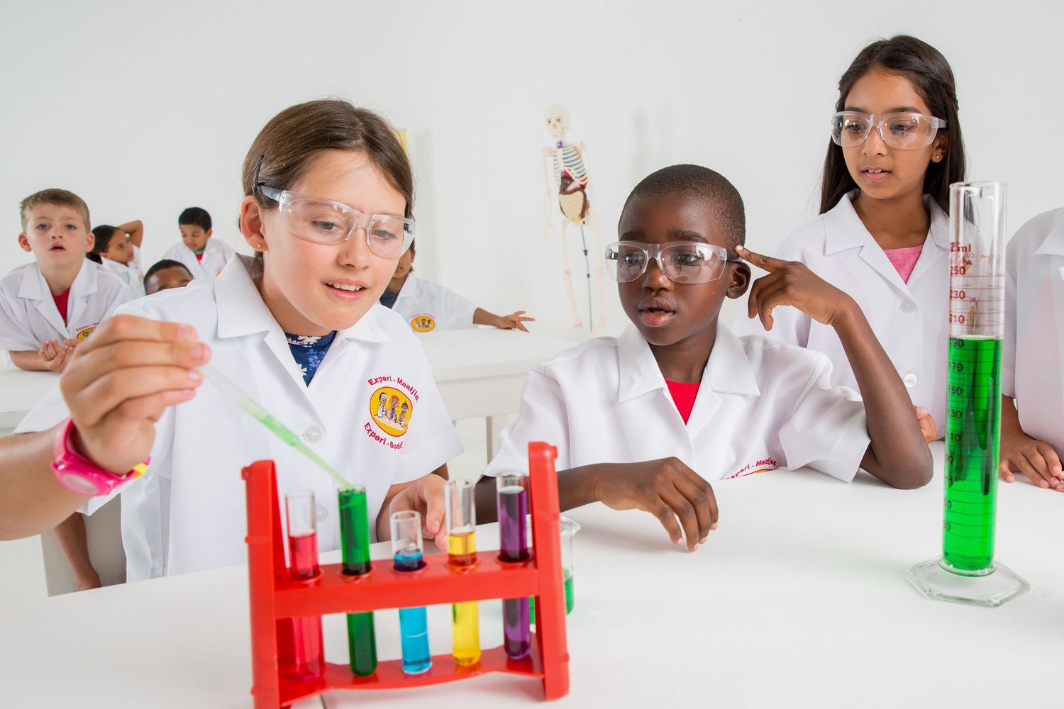 Students in lab coats conduct chemistry experiments using colorful test tubes in red rack.