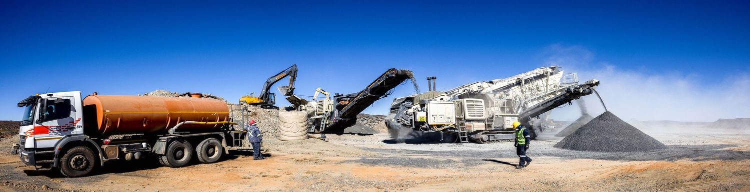 Large construction machinery and mobile crusher equipment working at an industrial site against blue sky.