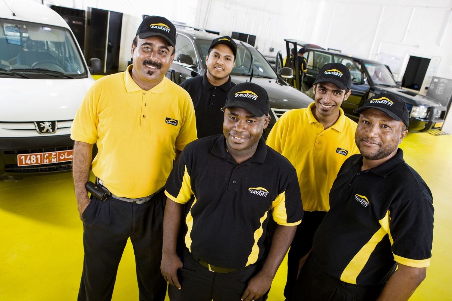 Service team members in yellow uniforms and black pants gathered outside automotive center.
