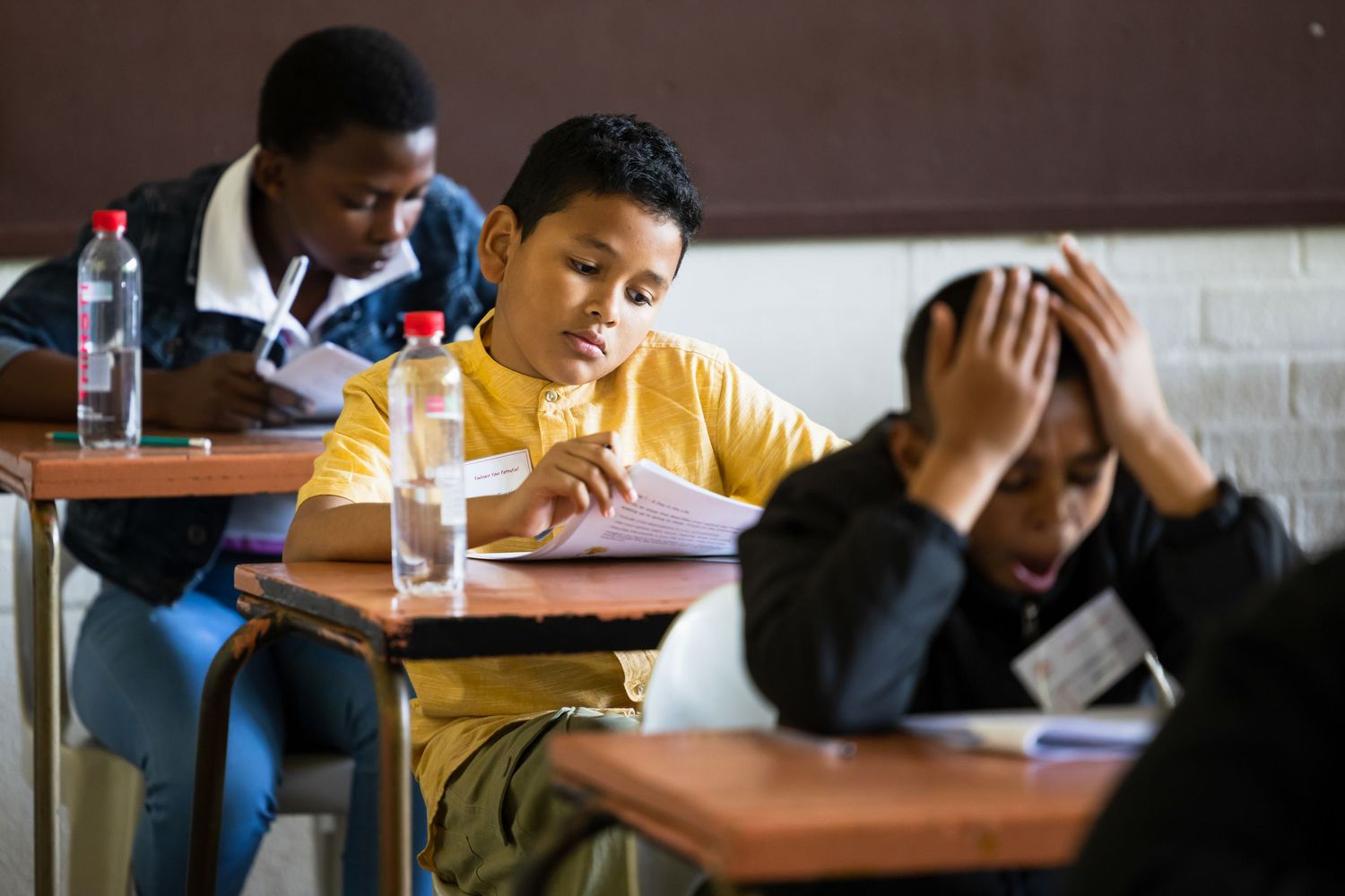 Students writing and studying at their desks in a dimly lit classroom.