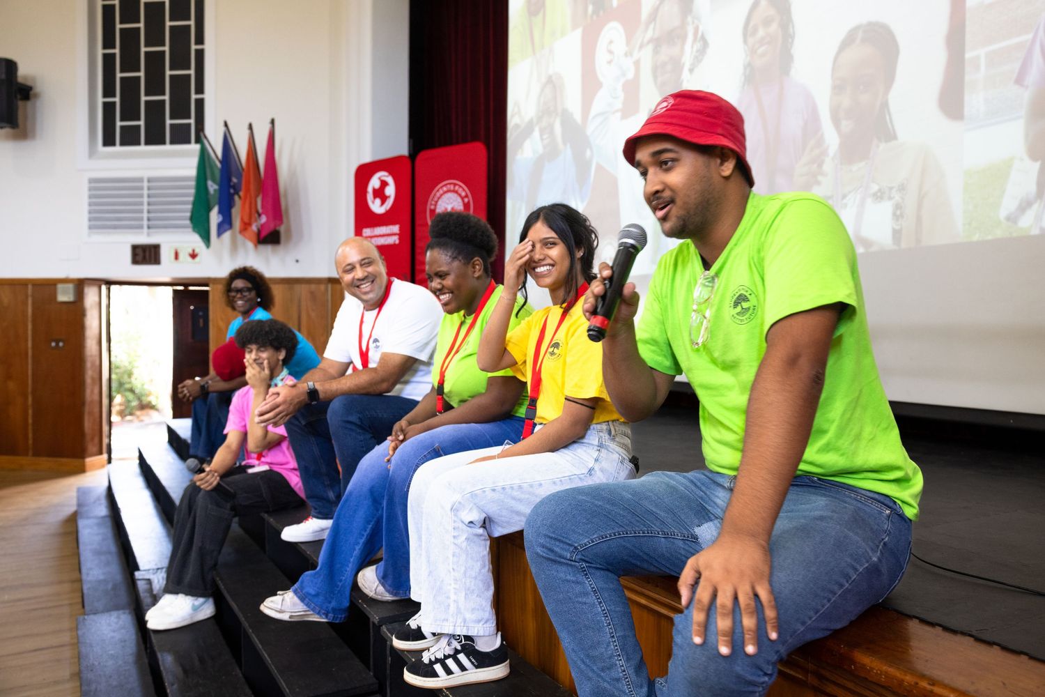 A group of people sit together watching a presentation in a community center or meeting room.
