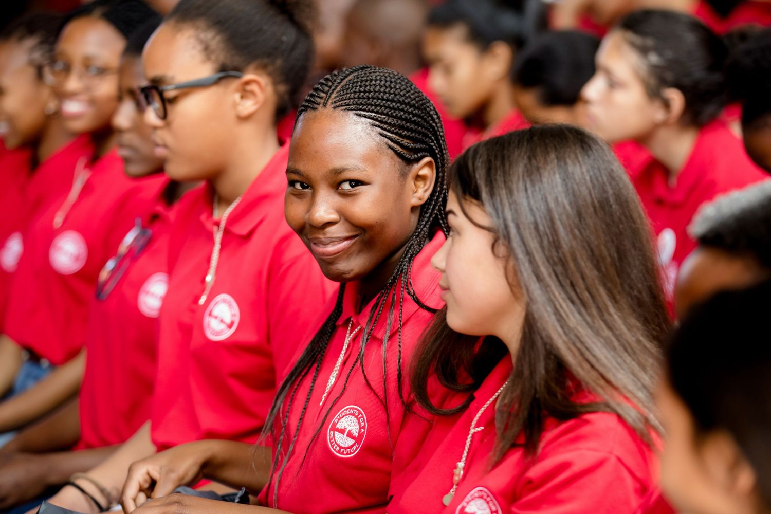 Students in red uniforms smile and interact during a group gathering.