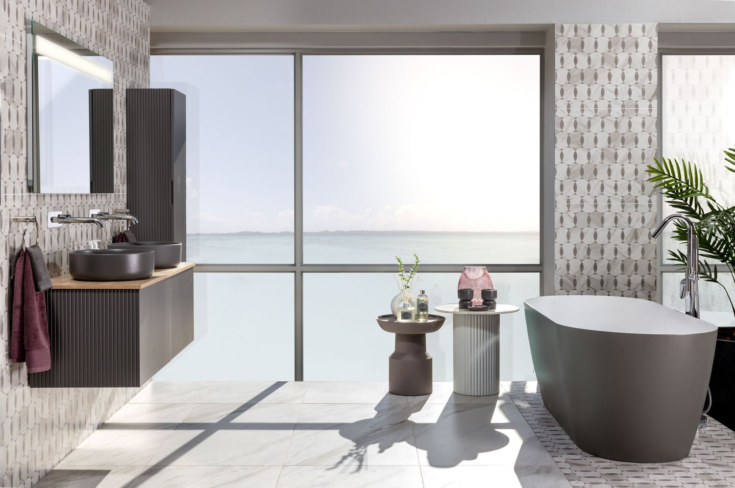 Contemporary bathroom with freestanding grey tub, textured walls, and floor-to-ceiling windows overlooking ocean view.